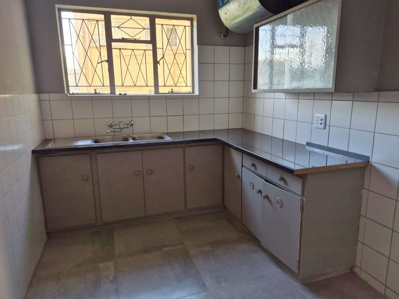 A functional kitchen featuring built-in cabinetry, laminate countertops, a double sink, and tiled splashbacks, offering a blank canvas for potential modern updates.