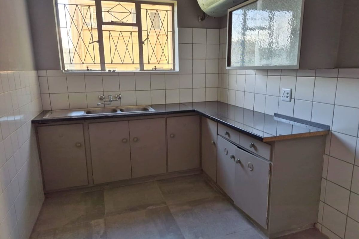 A functional kitchen featuring built-in cabinetry, laminate countertops, a double sink, and tiled splashbacks, offering a blank canvas for potential modern updates.