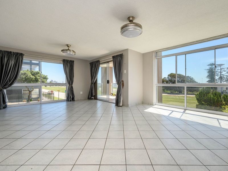 Spacious, light-filled living area featuring neutral tiled flooring, large windows, and sliding glass doors leading to an outdoor space.