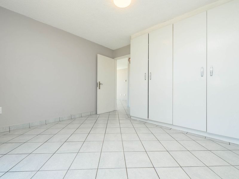 A clean, empty bedroom featuring neutral tiled flooring and ample built-in cupboard storage space.