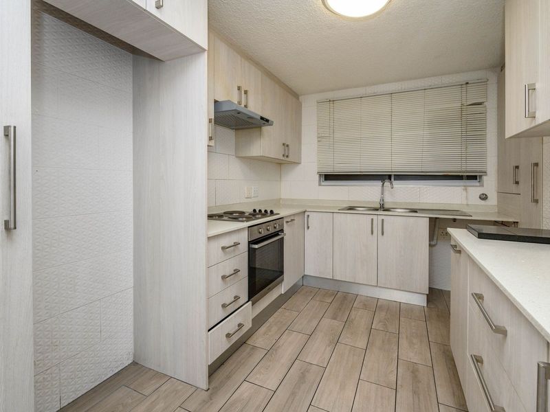 A clean, functional kitchen featuring light wood-tone cabinetry, stone-look countertops, integrated appliances, and durable wood-look tile flooring.