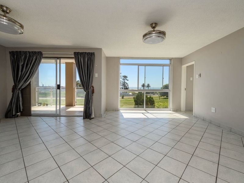Spacious, light-filled living area featuring neutral tiled flooring, ceiling fans, and large windows with access to a private balcony.