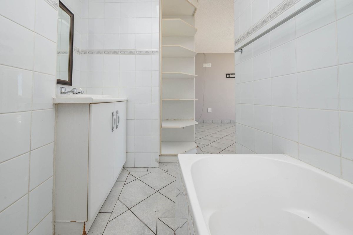 A functional bathroom featuring a vanity cabinet, built-in shelving, and a bathtub, finished with white wall tiles and neutral floor tiling.