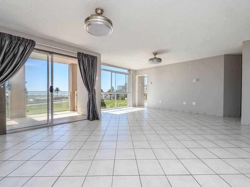 Spacious, light-filled living area featuring neutral tiled flooring, dual ceiling fans, and large sliding glass doors providing direct access to a private balcony.