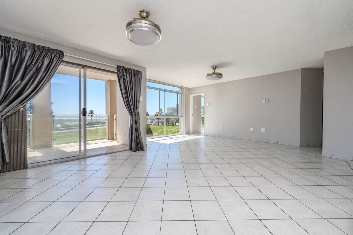 Spacious, light-filled living area featuring neutral tiled flooring, dual ceiling fans, and large sliding glass doors providing direct access to a private balcony.