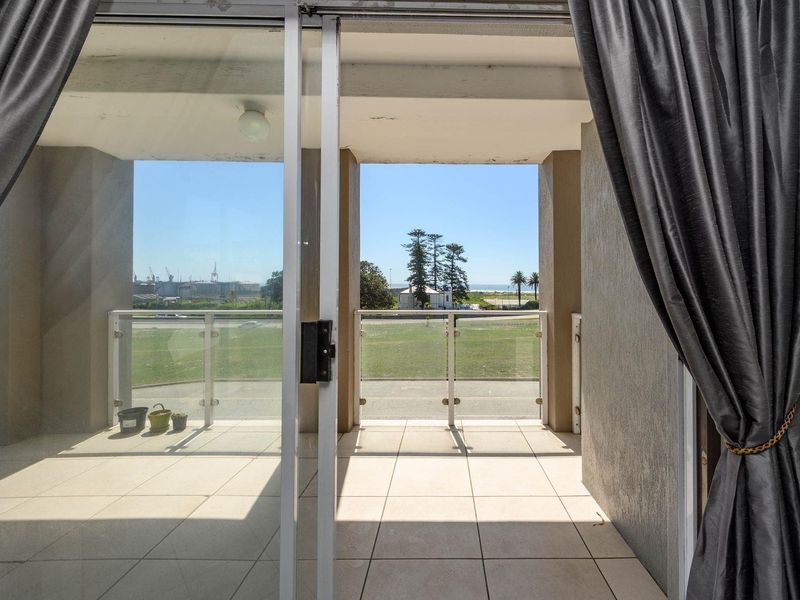 A covered balcony featuring tiled flooring and a modern glass balustrade, offering an open view of the surrounding area.