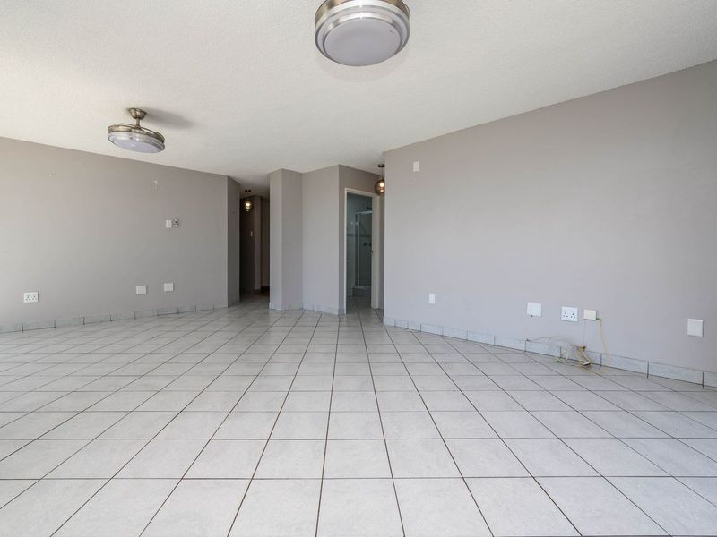 A spacious, empty living area featuring neutral grey walls, tiled flooring, and flush mount ceiling lighting, ready for personalization.