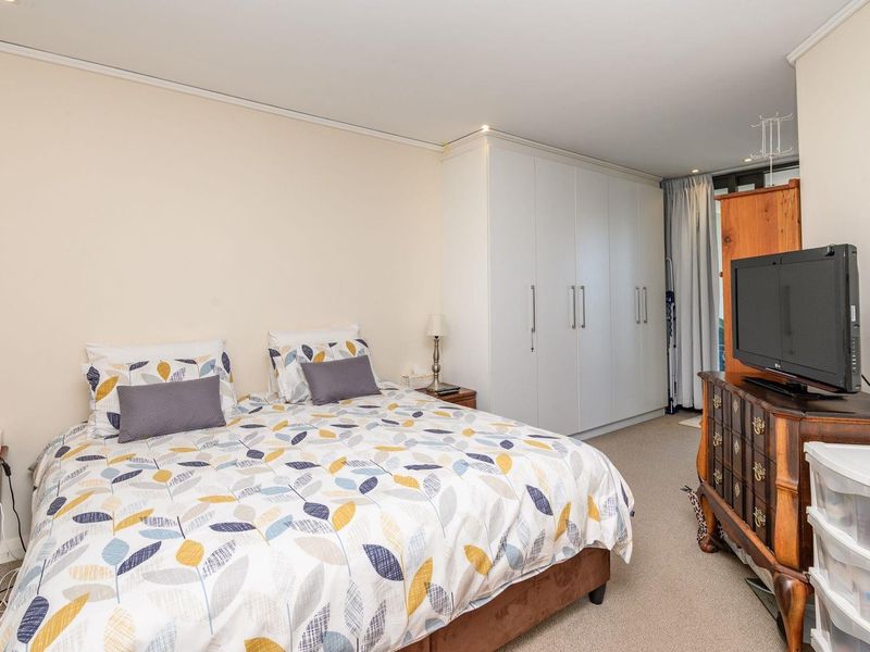 A well-proportioned bedroom featuring neutral walls, carpeted flooring, recessed lighting, and a large built-in wardrobe for ample storage.