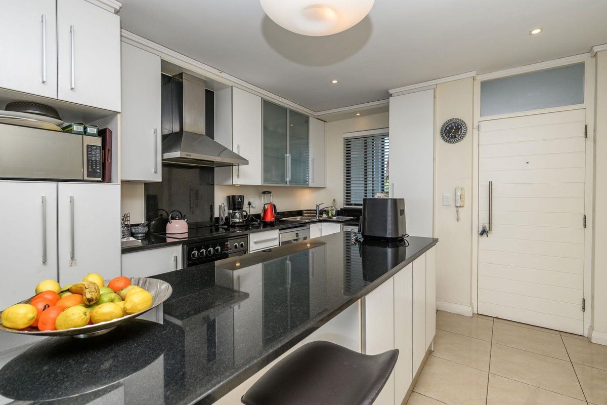 Modern kitchen featuring sleek white cabinetry, contrasting black granite countertops, integrated appliances, and a functional breakfast bar island.
