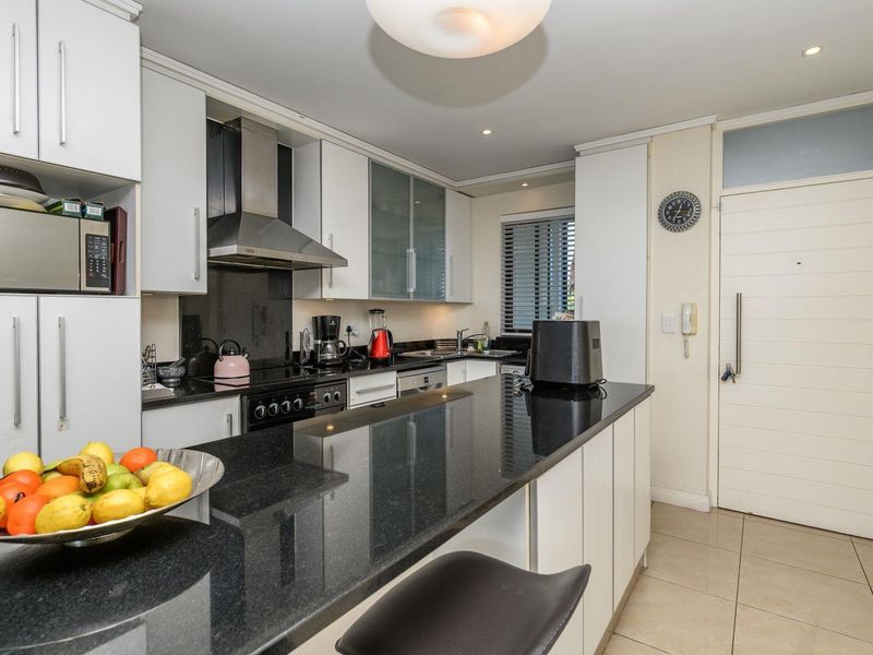 Modern kitchen featuring sleek white cabinetry, contrasting black granite countertops, integrated appliances, and a functional breakfast bar island.