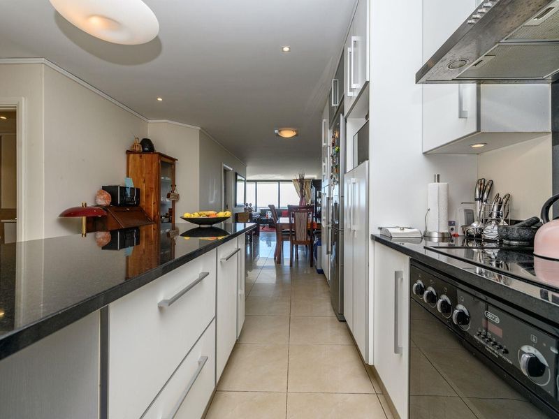 Modern kitchen featuring sleek white cabinetry, black granite countertops, integrated appliances, and tiled flooring, flowing into an open-plan living and dining area.