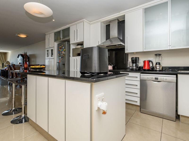 Modern open-plan kitchen featuring a central island with granite countertops, sleek white cabinetry, stainless steel appliances, and polished tiled flooring.