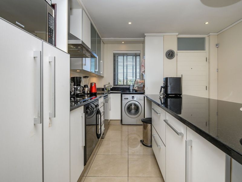 Modern kitchen featuring sleek white cabinetry, contrasting black granite countertops, integrated appliances, and tiled flooring, offering a functional and well-maintained workspace.