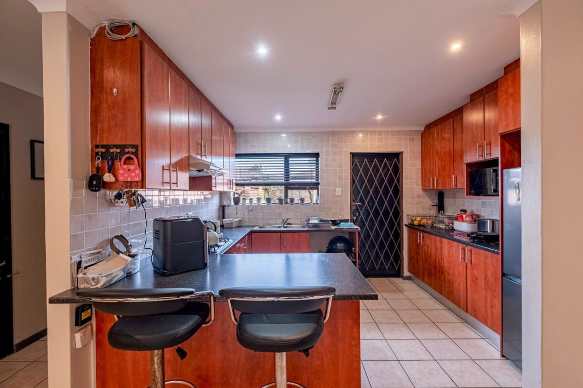 Functional kitchen featuring wood-veneer cabinetry, dark laminate countertops, a breakfast bar, tiled flooring, and a security gate leading to the exterior.