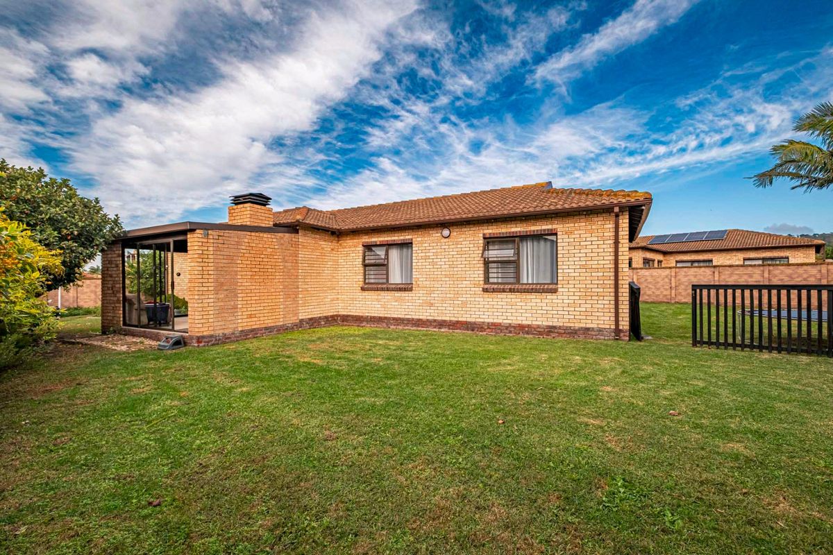 Rear view of the townhouse featuring face-brick exterior, tiled roof, enclosed patio area, and a private garden space.