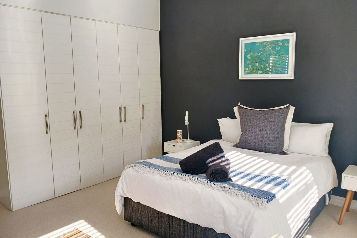 A well-maintained bedroom featuring a large wall-to-wall built-in wardrobe with white cabinetry and a striking dark accent wall.