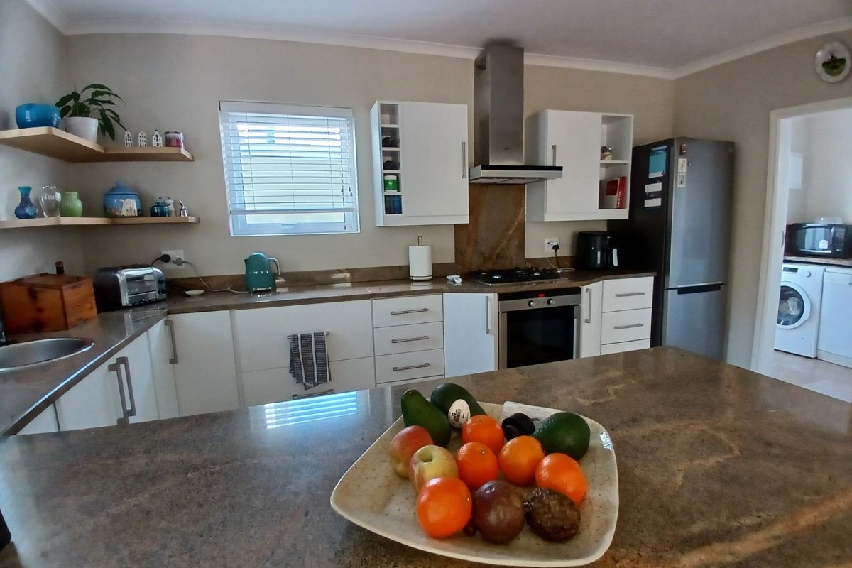 Modern kitchen featuring stone countertops, white cabinetry, stainless steel extractor fan, built-in oven, and a central island, with an adjacent laundry area visible.