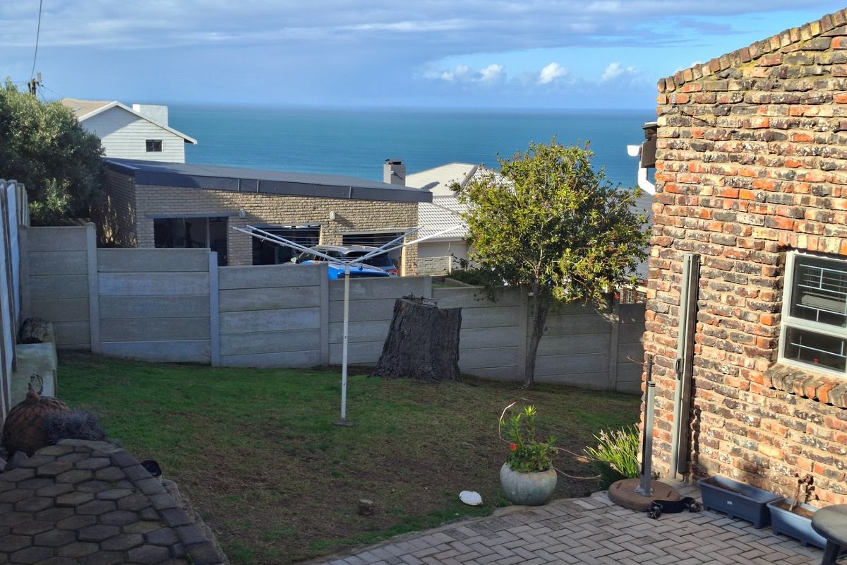A rear garden area featuring a paved patio, lawn, and precast concrete boundary wall, offering a scenic view of the ocean.