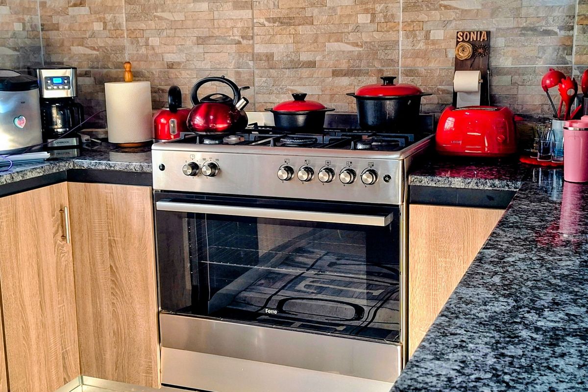 A functional kitchen area featuring a stainless steel gas stove, granite countertops, and textured stone-look wall tiling.