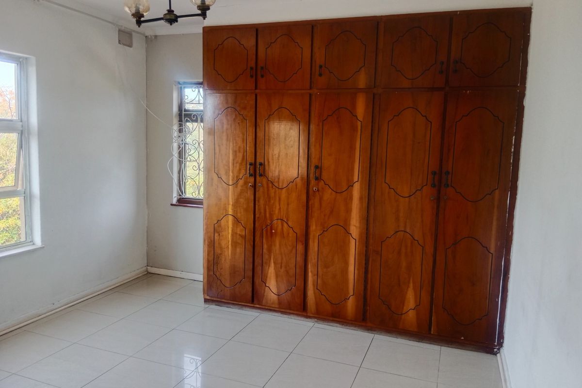 A vacant bedroom featuring tiled flooring and extensive built-in wooden cabinetry, offering ample storage space.