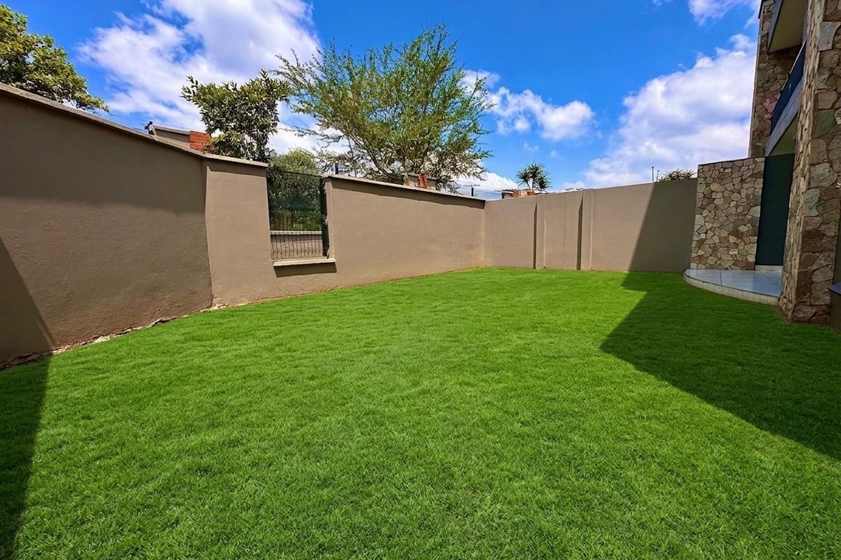 A well-maintained private rear garden featuring a lush green lawn, enclosed by high boundary walls and accented with stone cladding on the building exterior.