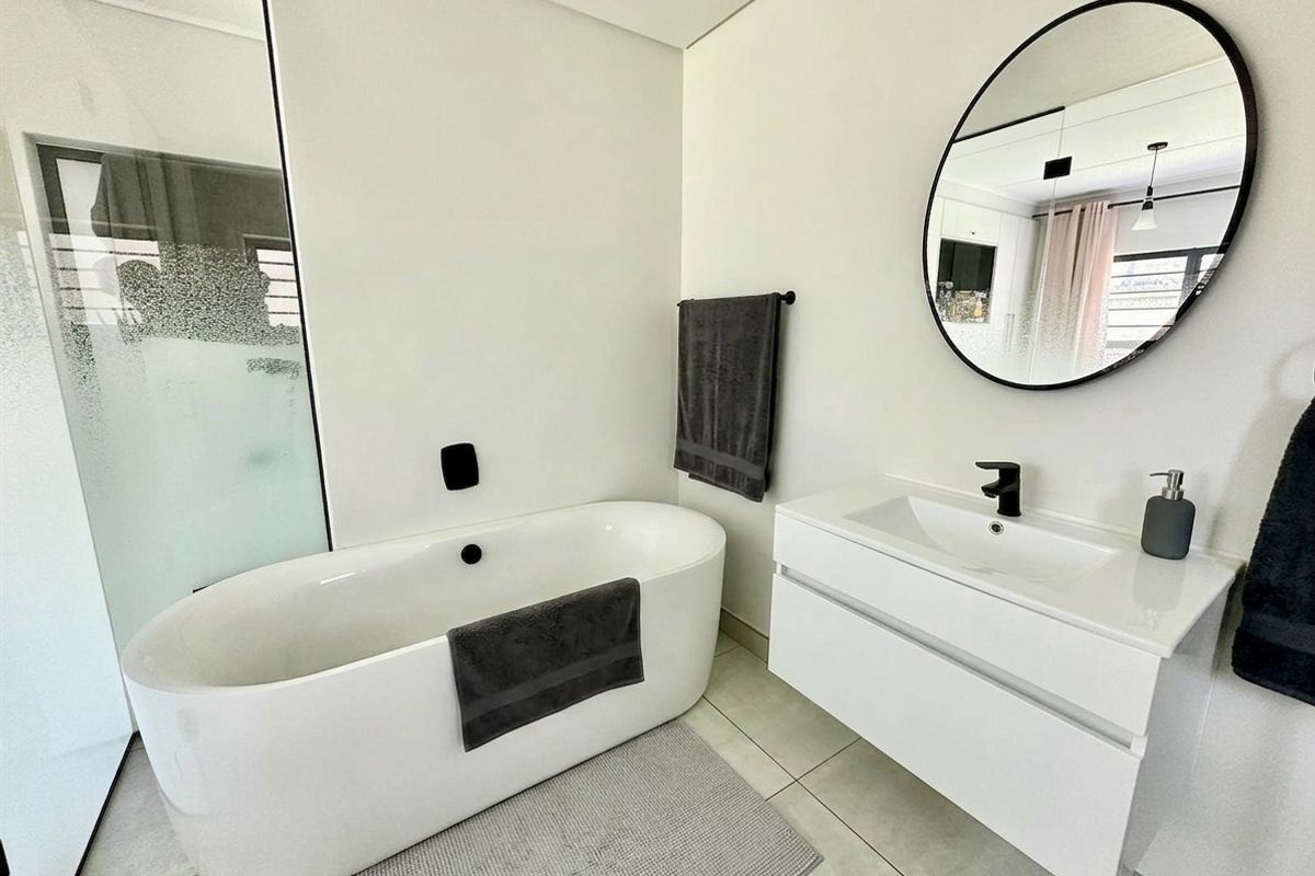 Modern bathroom featuring a sleek freestanding bathtub, floating vanity with integrated sink, and contemporary black matte fixtures.