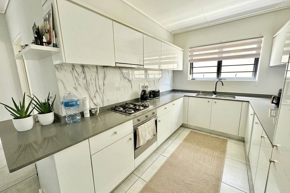 Modern kitchen featuring white gloss cabinetry, stone countertops, marble-look splashback, gas hob, built-in oven, and a sleek black mixer tap.
