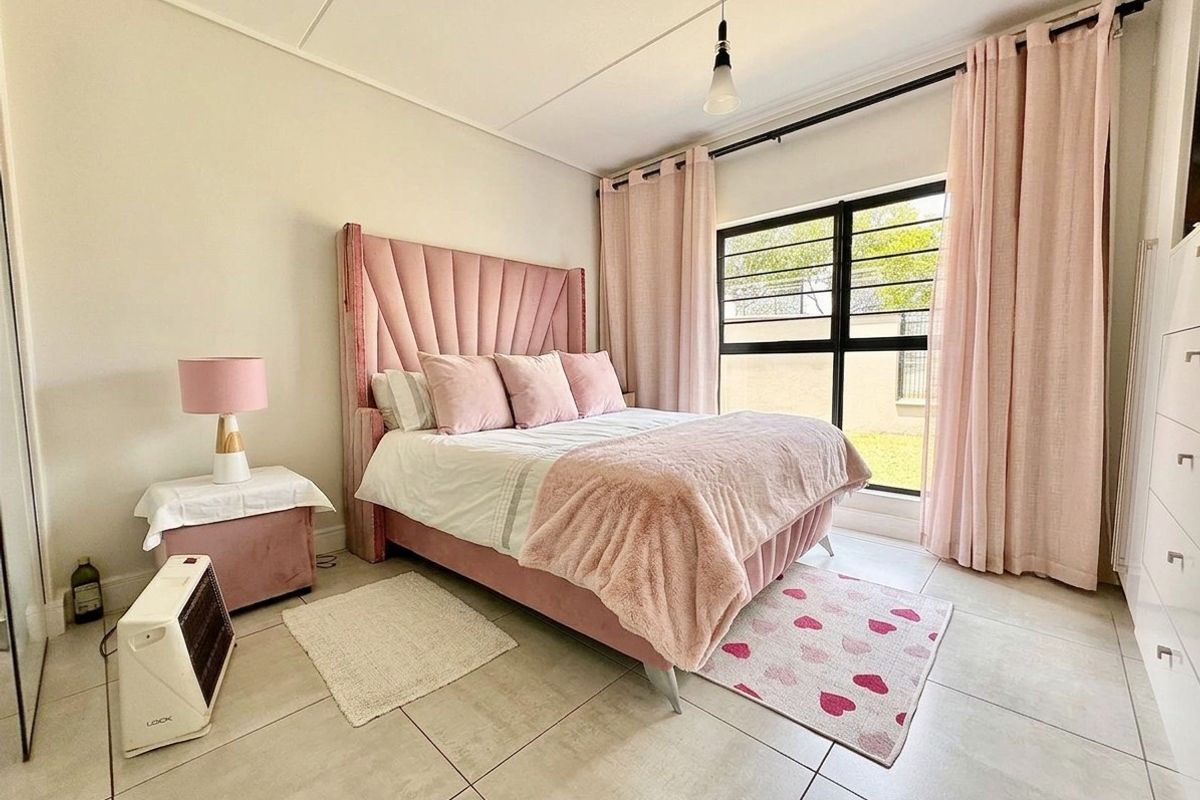 A well-lit bedroom featuring neutral tiled flooring, a large window with security bars, and a built-in wardrobe.