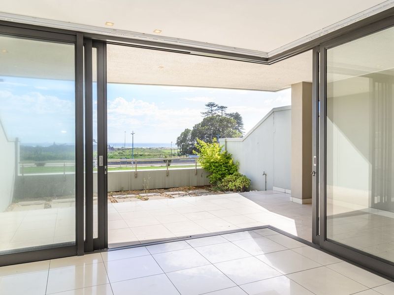 A spacious, covered balcony featuring modern tiled flooring, large sliding glass doors, and an open-plan layout with views of the surrounding area.