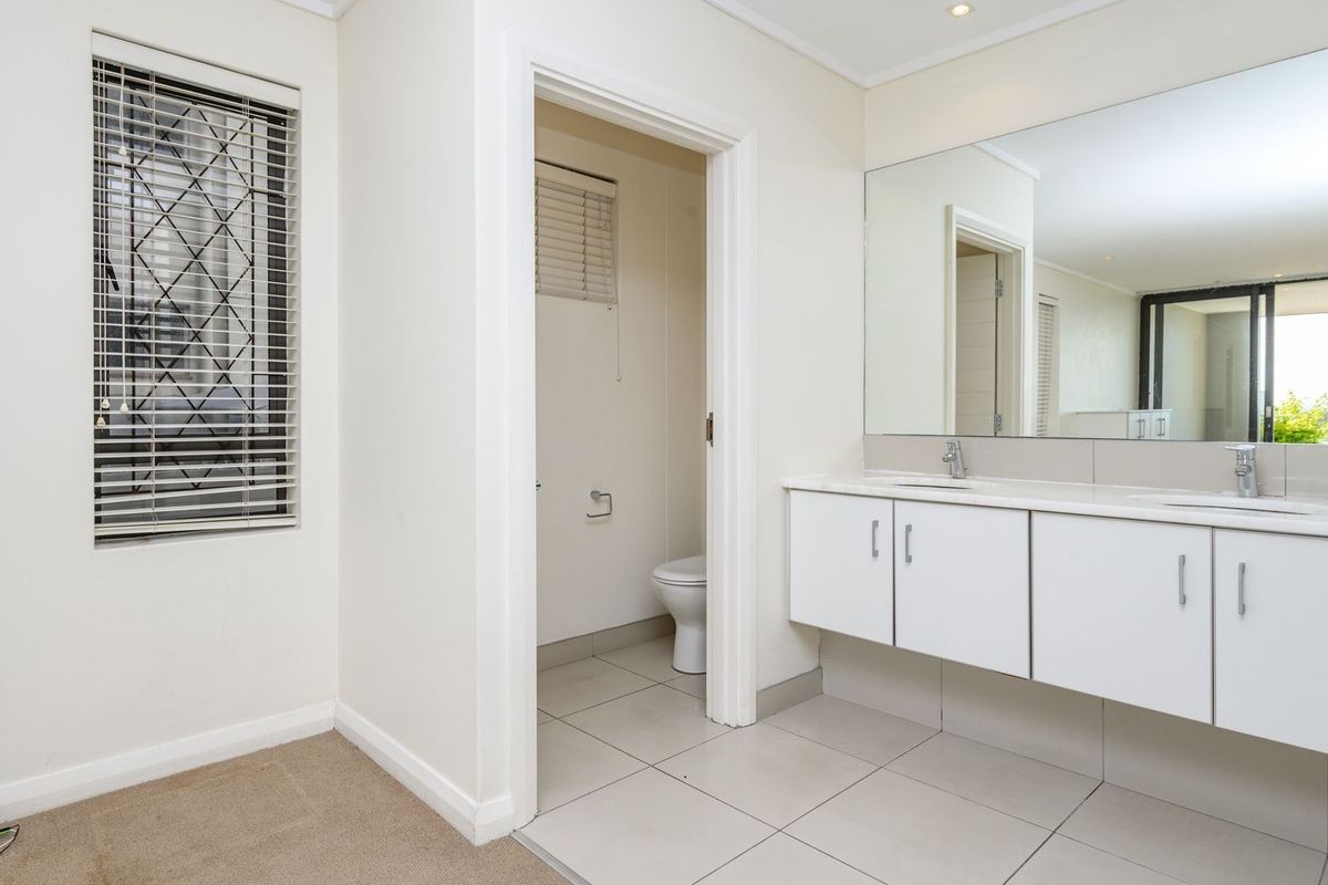 A clean, bright bathroom featuring a double vanity with white cabinetry, large wall mirror, tiled flooring, and a separate enclosed toilet area.