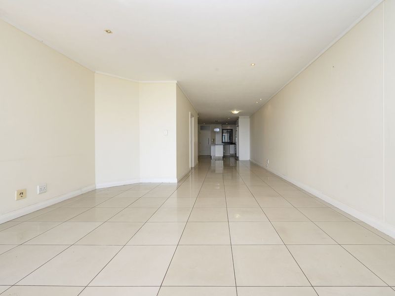 A spacious, empty open-plan living area featuring neutral walls, tiled flooring, and recessed lighting, offering a versatile blank canvas for interior design.