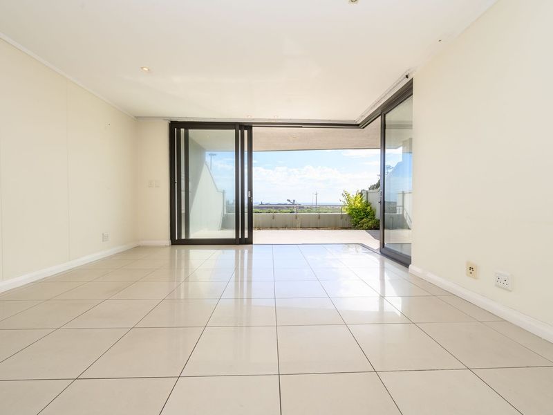 A bright, empty living room featuring large sliding glass doors that open onto a balcony with scenic views and tiled flooring throughout.