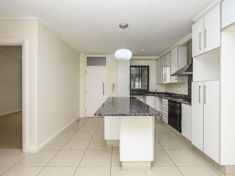 Modern kitchen featuring white cabinetry, granite countertops, a central island, and integrated appliances, finished with neutral floor tiles.