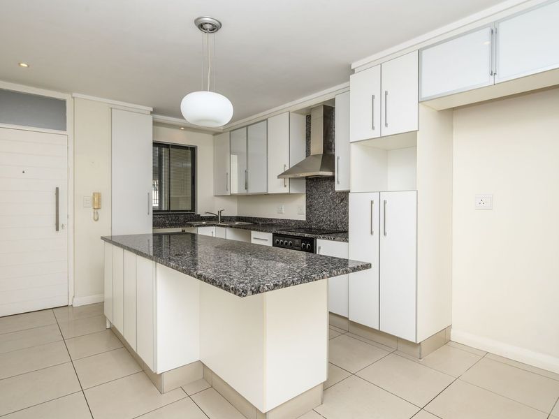 Modern kitchen featuring granite countertops, a central island, built-in cabinetry, and stainless steel appliances, finished with neutral ceramic floor tiles.