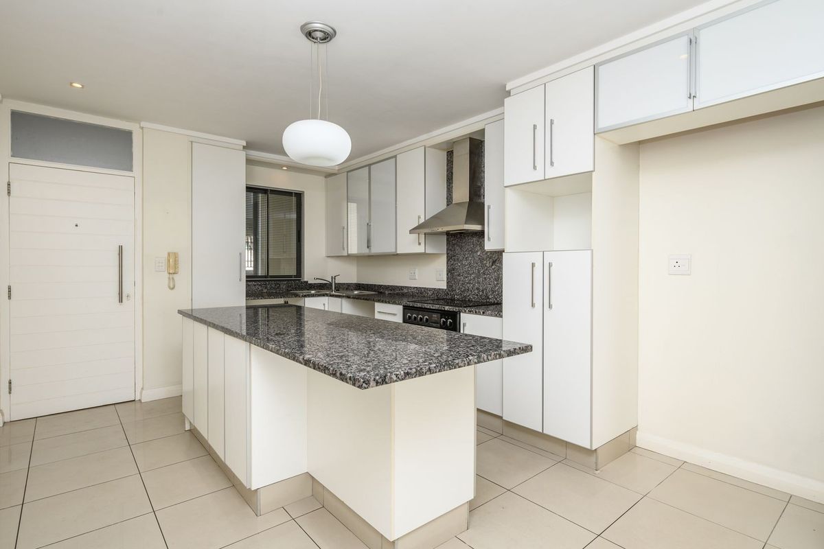 Modern kitchen featuring granite countertops, a central island, built-in cabinetry, and stainless steel appliances, finished with neutral ceramic floor tiles.