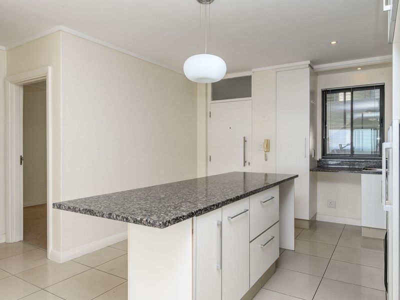 A clean, modern kitchen featuring a central granite-topped island, ample built-in cabinetry, and neutral tiled flooring in an open-plan layout.