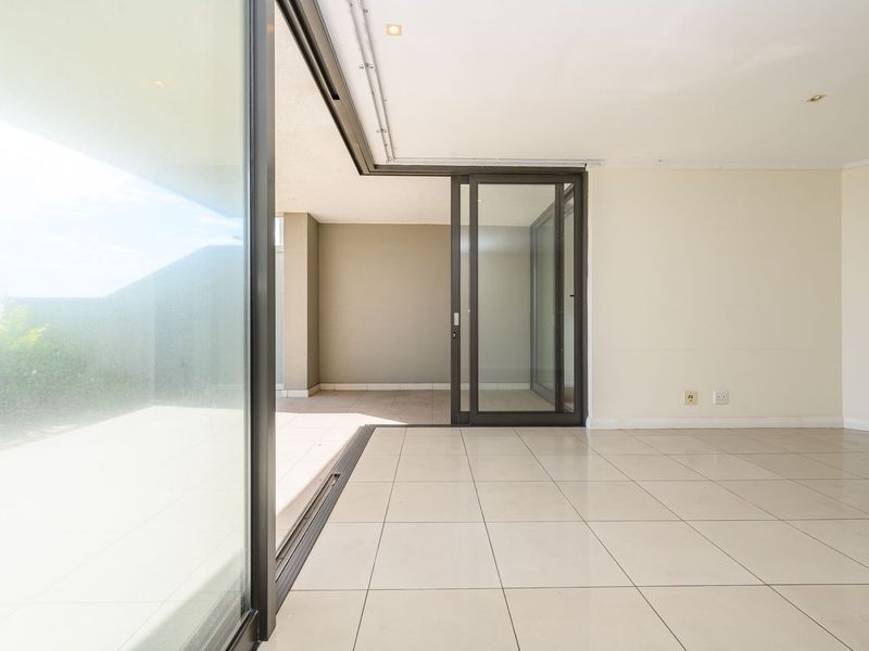 Bright and spacious living area featuring large sliding glass doors that open onto a covered patio, finished with neutral floor tiles and recessed lighting.