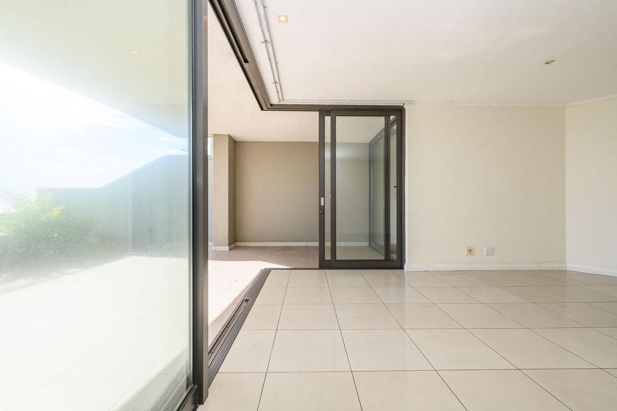 Bright and spacious living area featuring large sliding glass doors that open onto a covered patio, finished with neutral floor tiles and recessed lighting.
