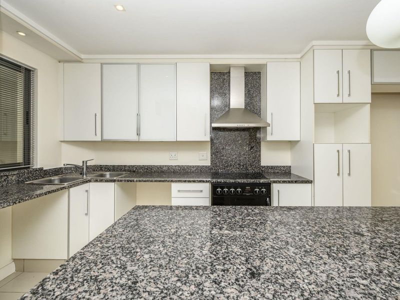 A clean, functional kitchen featuring granite countertops, ample white cabinetry, a stainless steel extractor fan, and a freestanding oven.