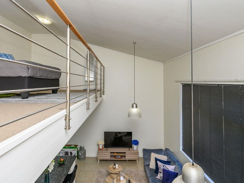 Open plan living area featuring a mezzanine bedroom level with a modern stainless steel balustrade, high ceilings, and large windows providing natural light.
