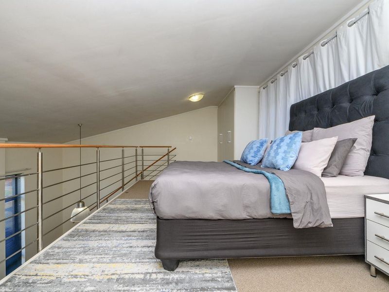 A loft-style bedroom featuring a mezzanine level with a stainless steel balustrade, built-in cupboards, and a sloped ceiling.