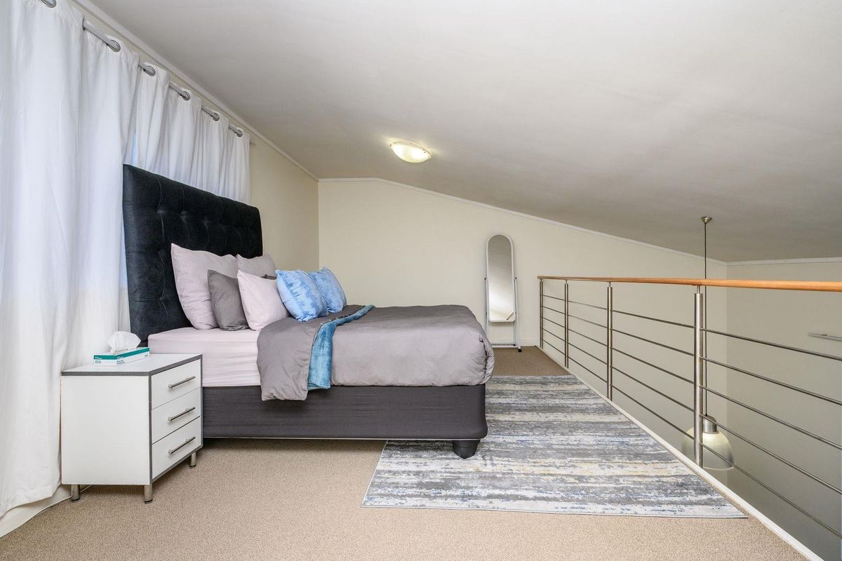 A loft-style bedroom featuring a sloped ceiling, carpeted flooring, and a modern stainless steel balustrade overlooking the lower level.