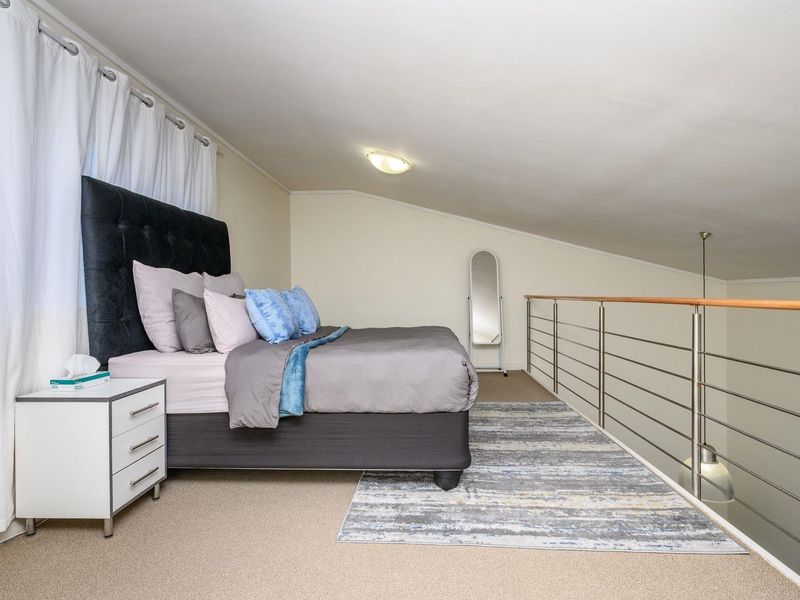 A loft-style bedroom featuring a sloped ceiling, carpeted flooring, and a modern stainless steel balustrade overlooking the lower level.