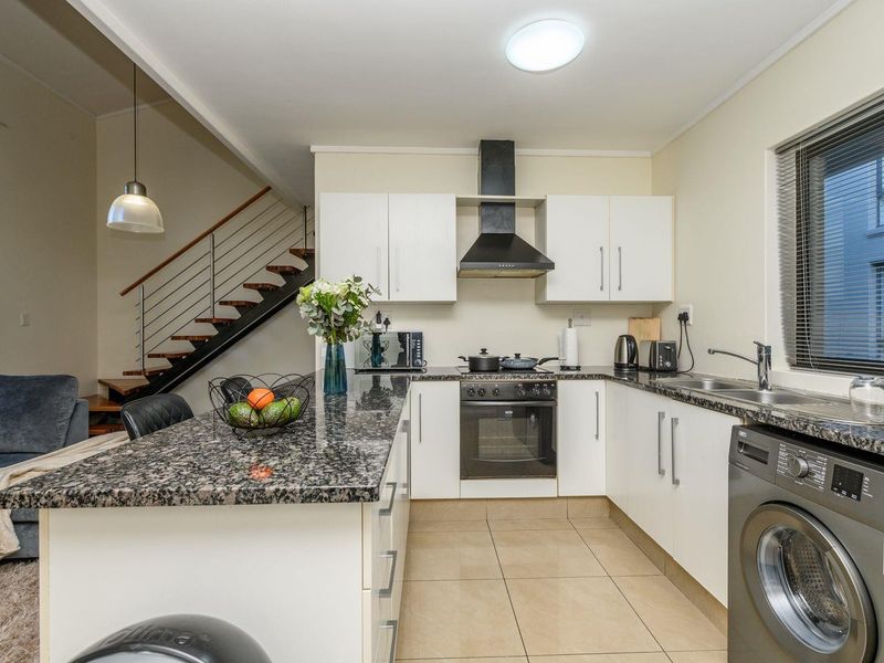 Open-plan kitchen featuring granite countertops, built-in oven, extractor fan, and tiled flooring, seamlessly connected to the living area and staircase.