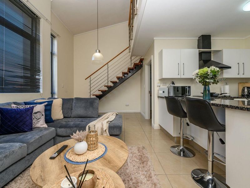 Open-plan living area featuring a modern staircase with stainless steel balustrade, tiled flooring, and a functional kitchen with granite countertops.