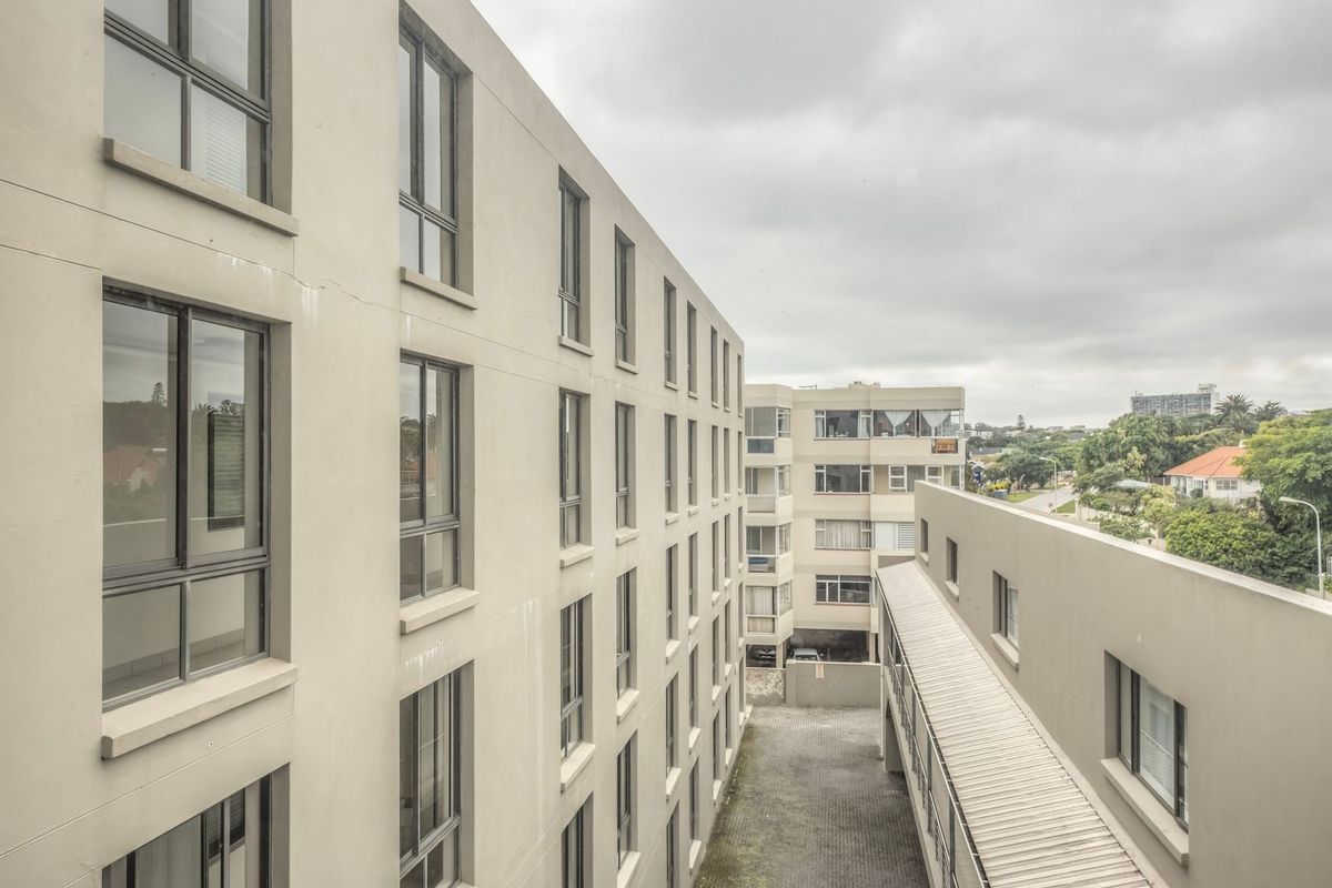 Exterior view of the apartment complex showing the rear facade, paved courtyard area, and covered walkway between building blocks.