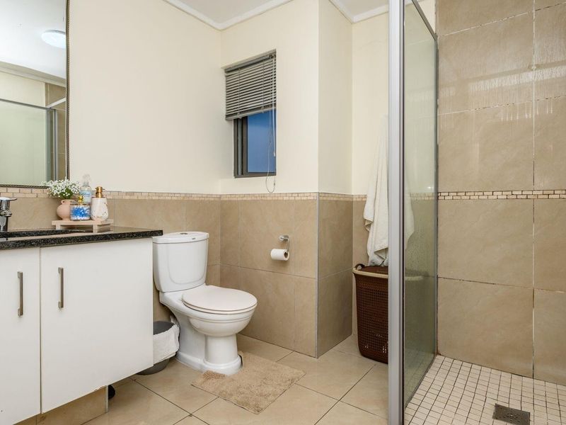 A functional bathroom featuring a vanity with granite countertop, a toilet, and a walk-in shower with glass enclosure and tiled finishes.