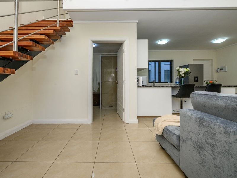 Open plan living area featuring a modern floating staircase with stainless steel balustrades, tiled flooring, and a functional kitchen with granite countertops.