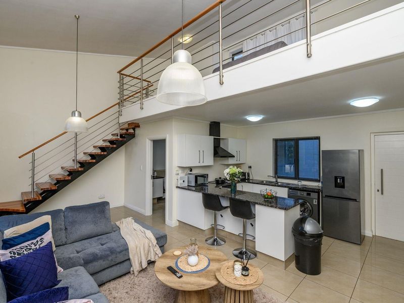 Open-plan living area featuring a modern kitchen with granite countertops, a mezzanine level, and a staircase with a contemporary metal railing.