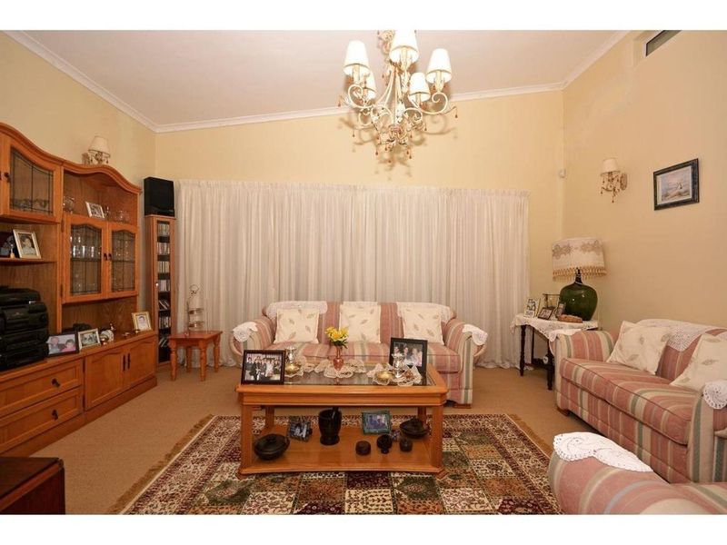 A traditional living room featuring a central chandelier, coved ceilings, and carpeted flooring, providing a comfortable and classic living space.